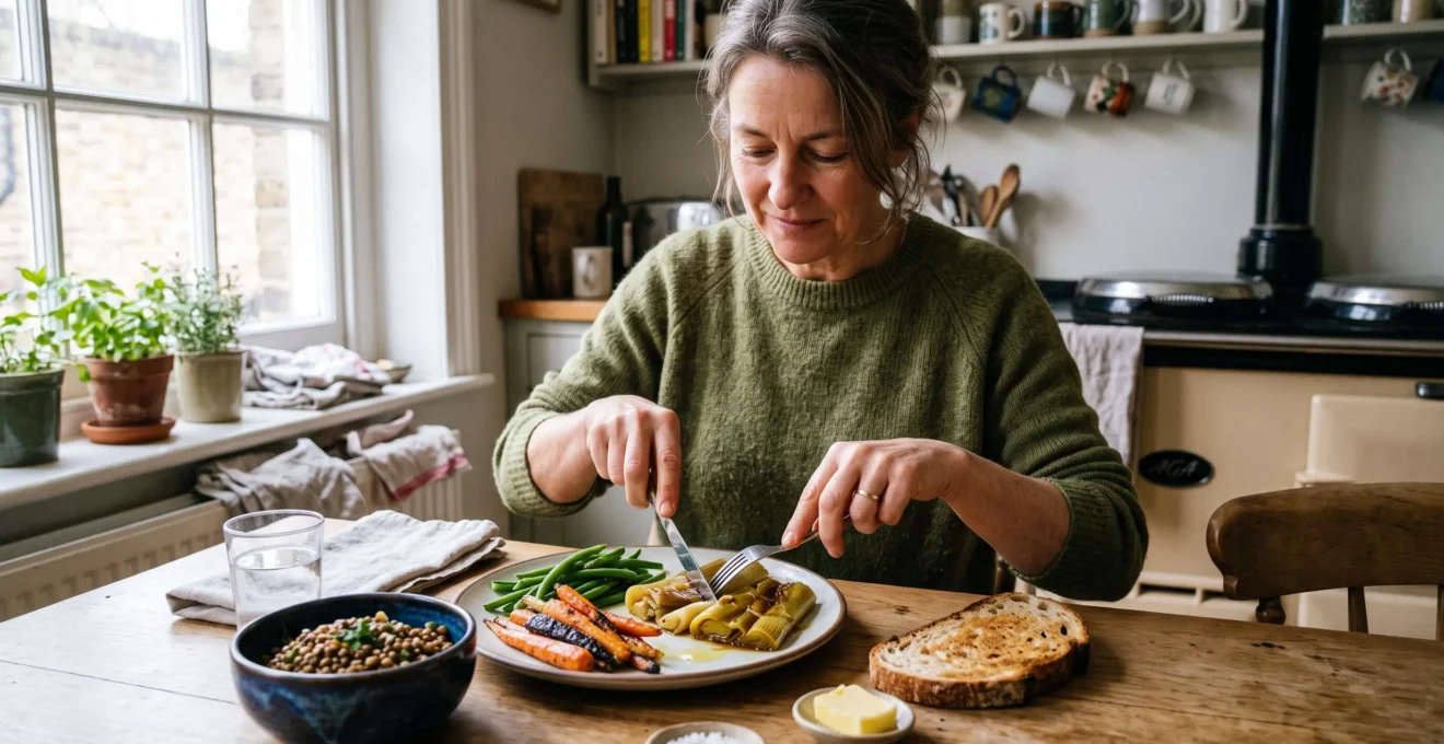 Une femme déguste à table une assiette de légumes cuits riches en fibres accompagnés de lentilles et de pain au levain, dans une cuisine lumineuse.